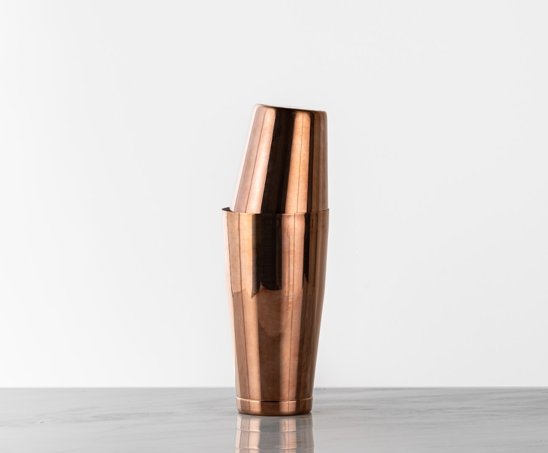 Antique copper cocktail shaker, deep bronze color, stacked on a marble countertop