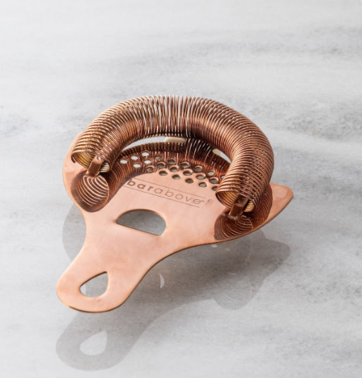 Antique copper bronze colored Hawthorne strainer lying flat on a white marble counter