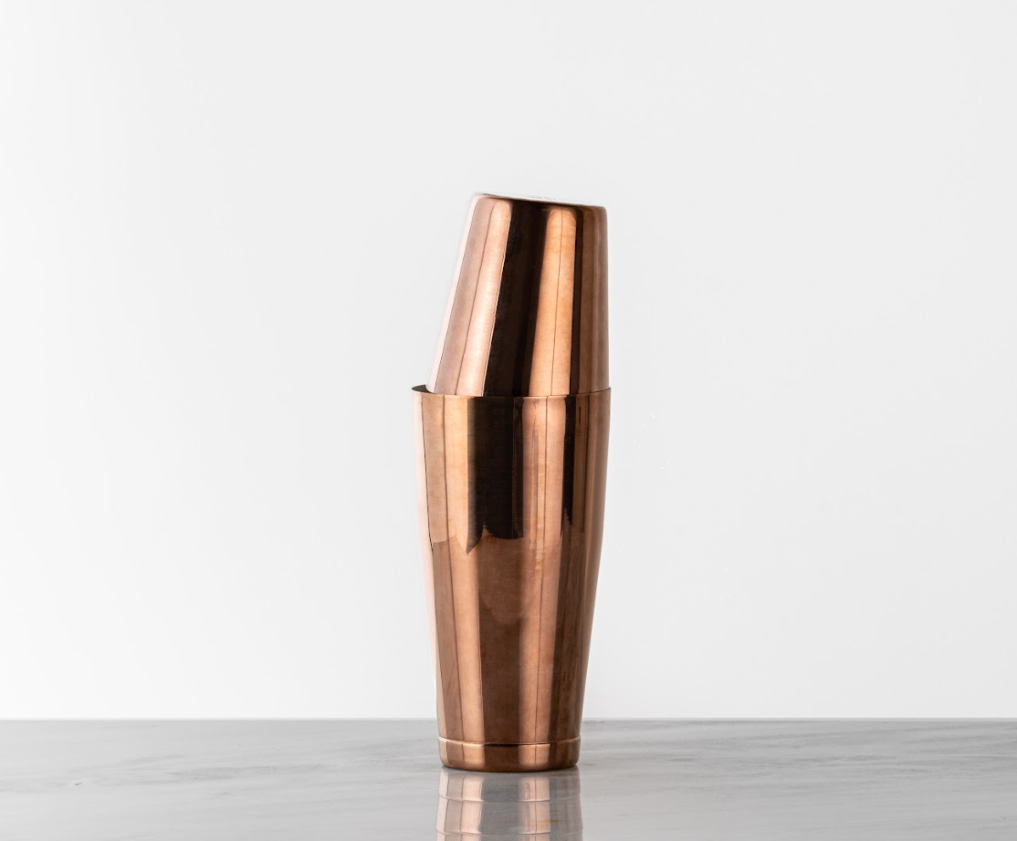Antique copper cocktail shaker, deep bronze color, stacked on a marble countertop 