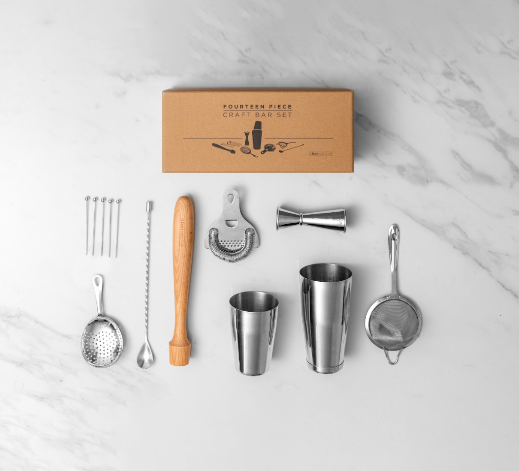 Top down photo of a gift box that says "14 piece craft bar set" surrounded by picks, 3 strainers, muddler, spoon, jigger, & cocktail shaker