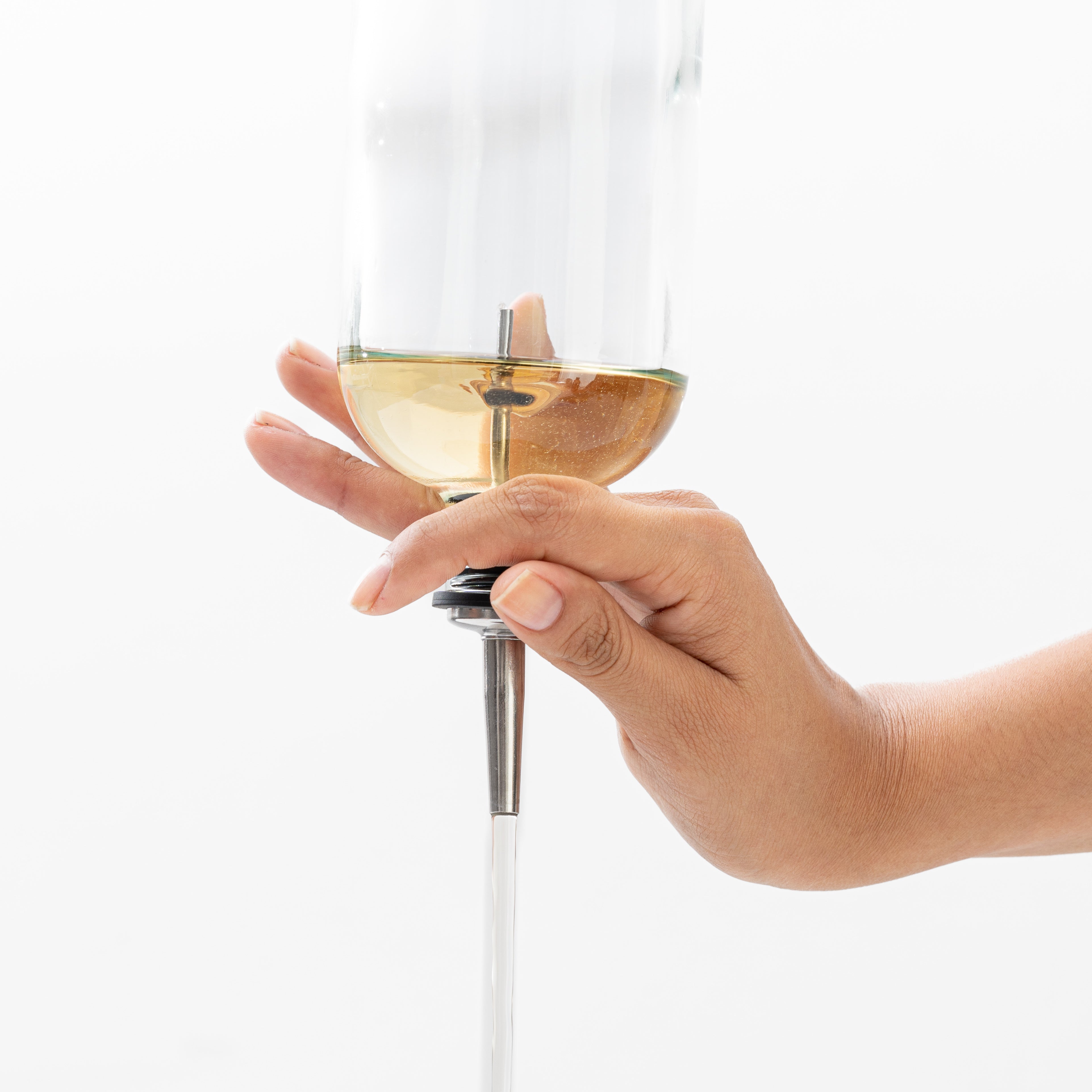 Hand holding a clear bottle with champagne-colored liquid upside down, with liquid coming out a stainless steel pour spout