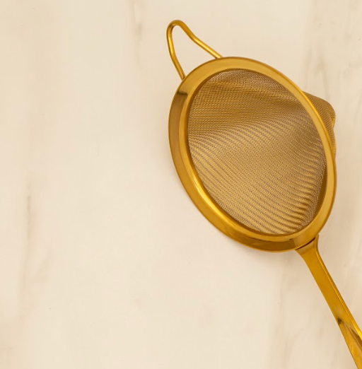 Gold fine mesh strainer lying on a white marble table