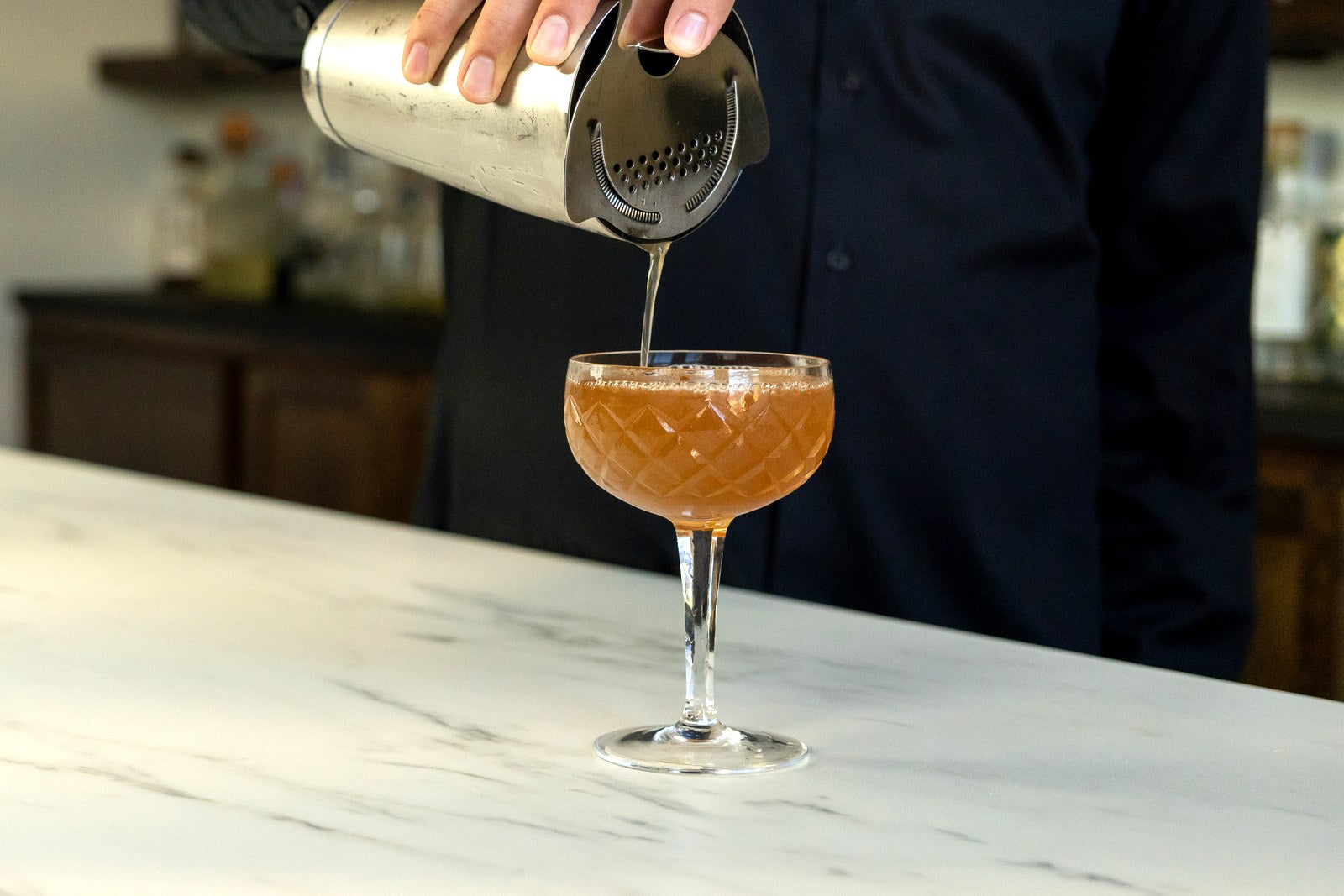 Straining a cocktail through a Hawthorne strainer from a Boston shaker tin into a coupe glass