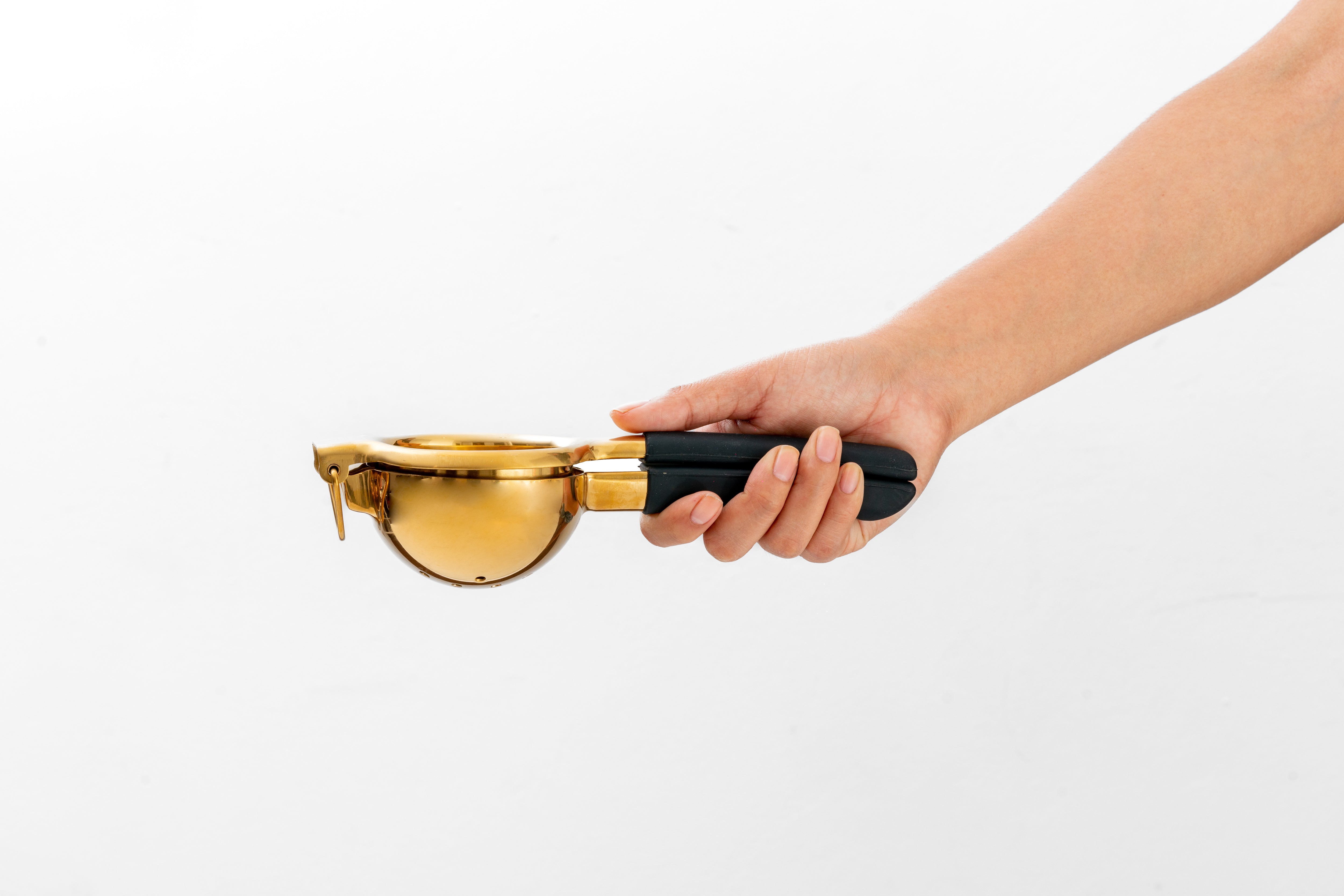 Hand holding a gold lemon juicer with black silicone handles, set against a white backdrop