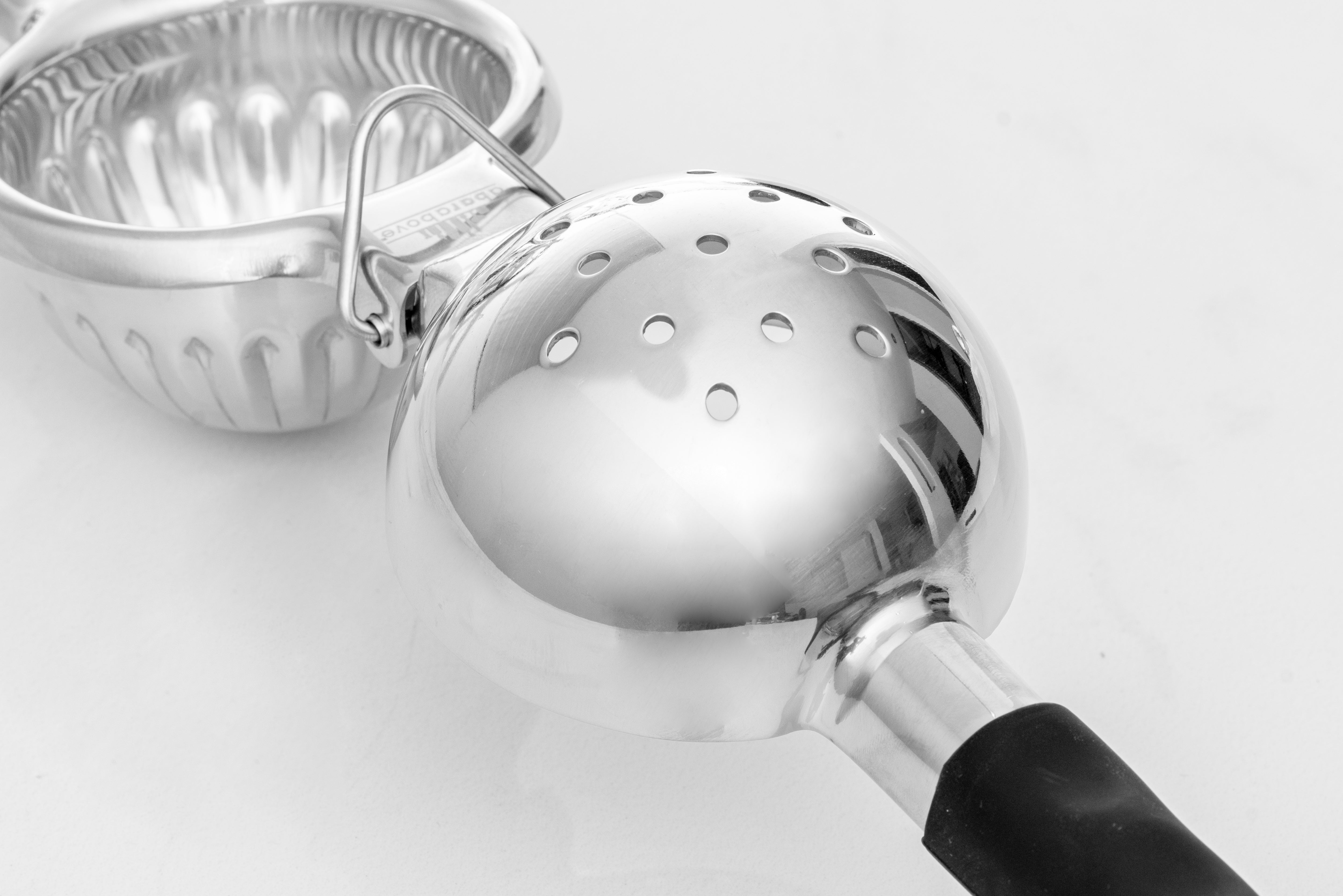 Stainless steel citrus juicer lying open on a white background, showing the holes where the juice filters through